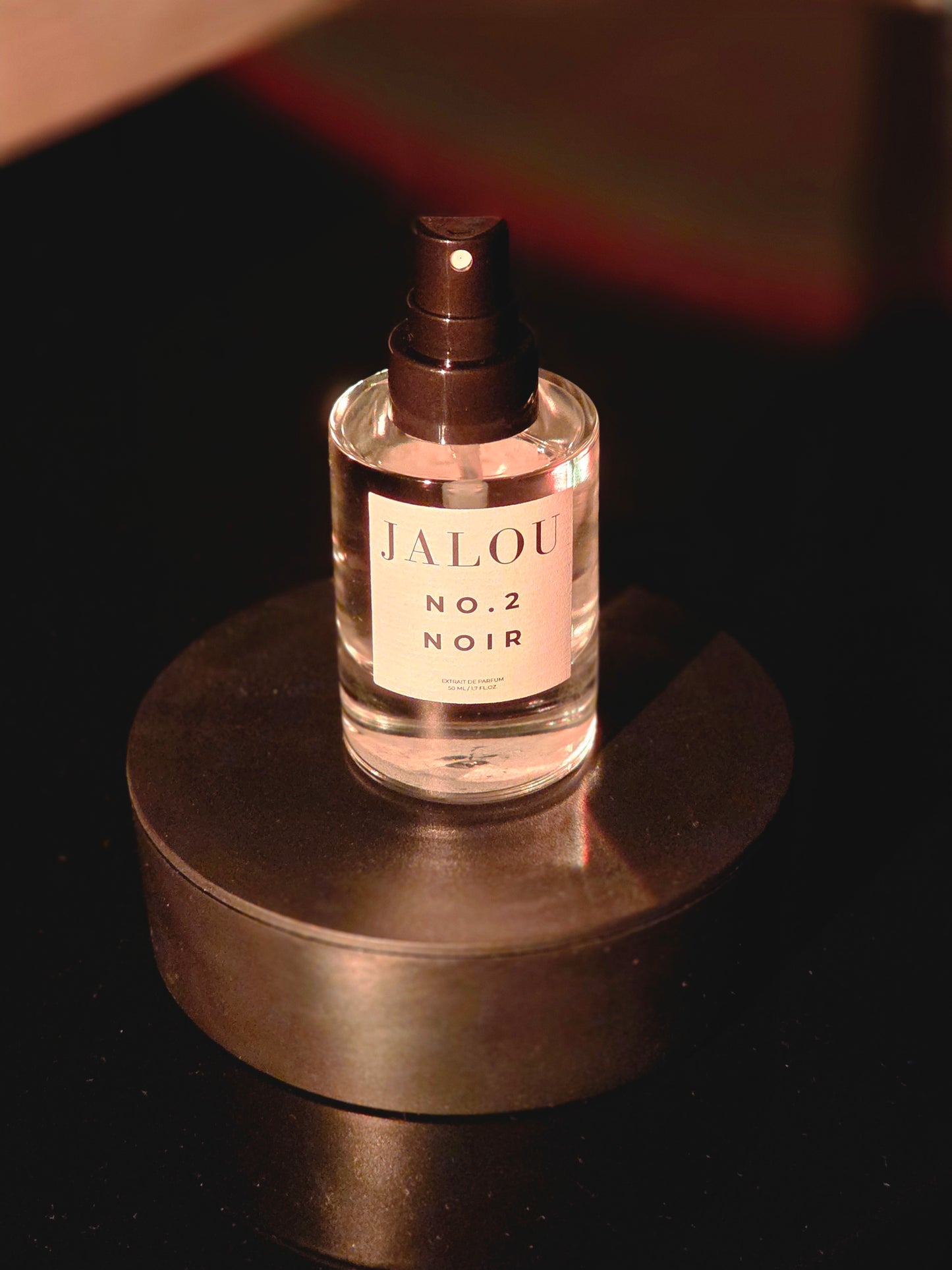 JALOU NO.2 NOIR Extrait de Parfum 50ml Flakon auf einem schwarzen Sockel mit dichten, erdigen und dunklen Rauchschwaden im Hintergrund.