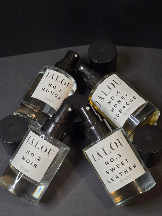 Vier Parfumflakons mit Sprühaufsatz, beschriftet mit No. 1 Rouge, No. 2 Noir, No. 3 Sweet Leather und No. 4 Honey Tobacco, auf dunklem Hintergrund.