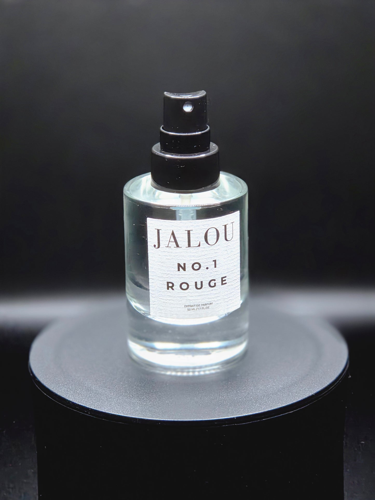 JALOU NO. 1 ROUGE Extrait de Parfum – Detailansicht des Flakons auf schwarzem Podest vor dunklem Hintergrund.