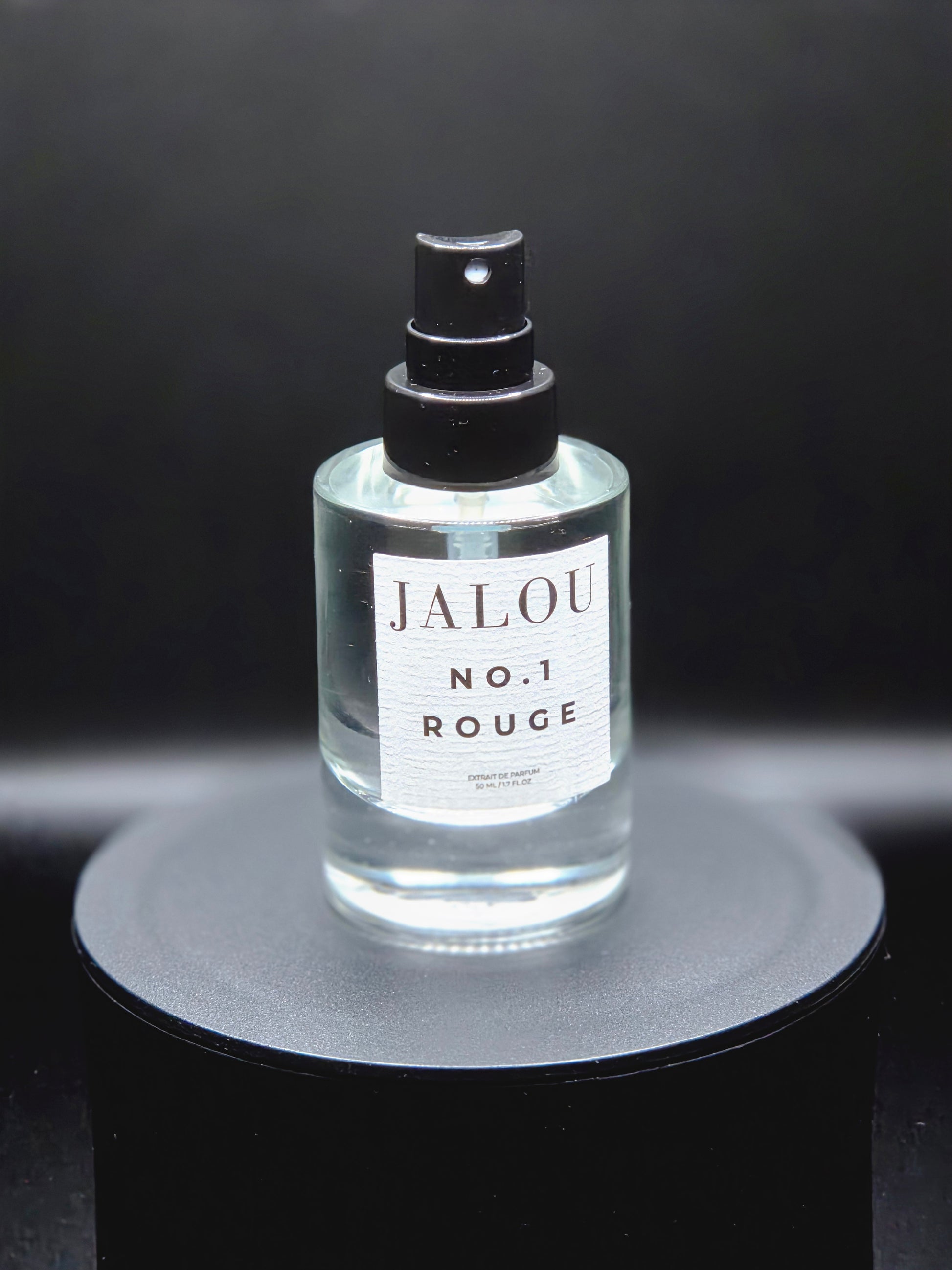 JALOU NO. 1 ROUGE Extrait de Parfum – Detailansicht des Flakons auf schwarzem Podest vor dunklem Hintergrund.