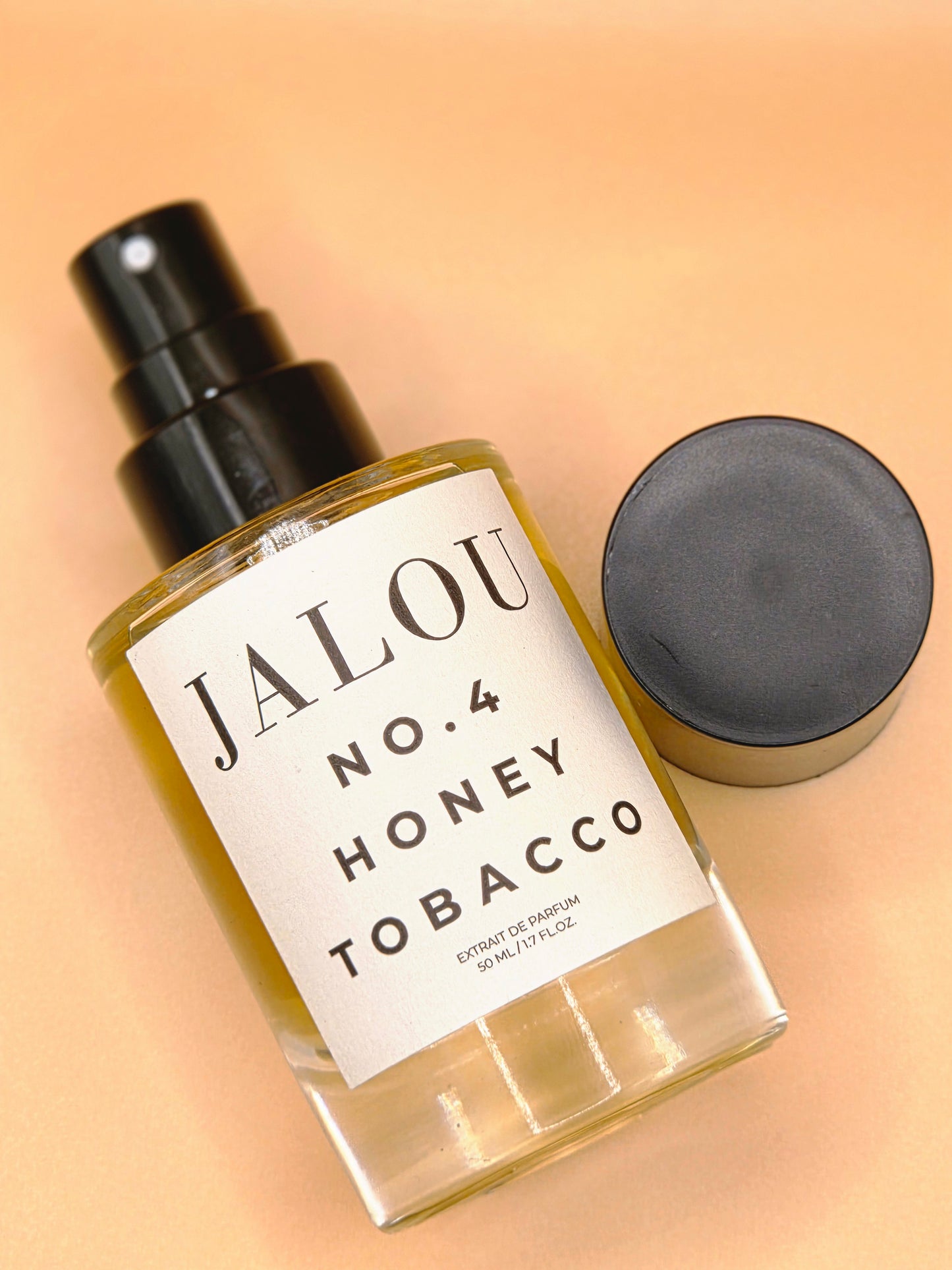 Schräge Ansicht eines JALOU NO. 4 HONEY TOBACCO Flakons mit abgenommenem Deckel auf einem beigefarbenen Hintergrund.