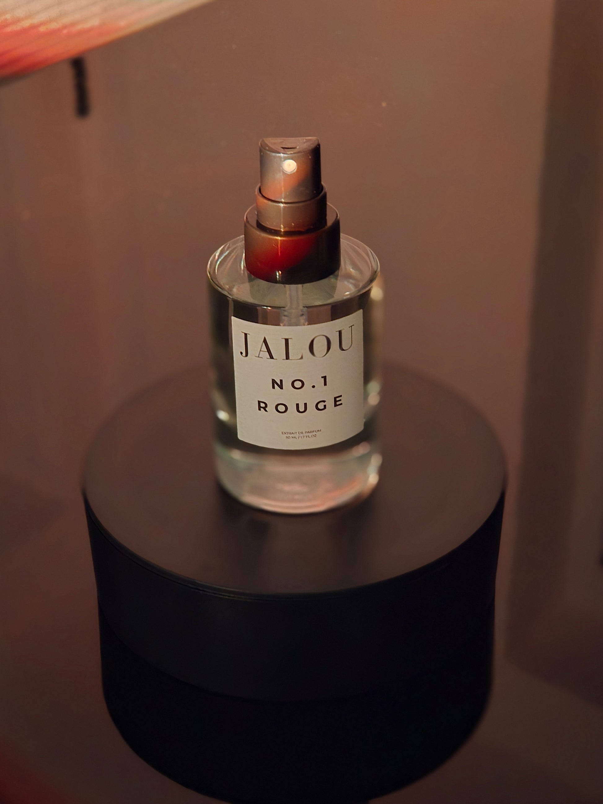 JALOU NO.1 ROUGE Extrait de Parfum 50ml Flakon auf einem schwarzen Sockel mit mystischen roten und goldenen Rauchschwaden im Hintergrund.
